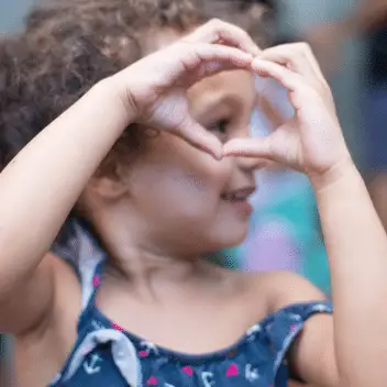 Criança sorridente com mãos unidas formando um gesto de coração